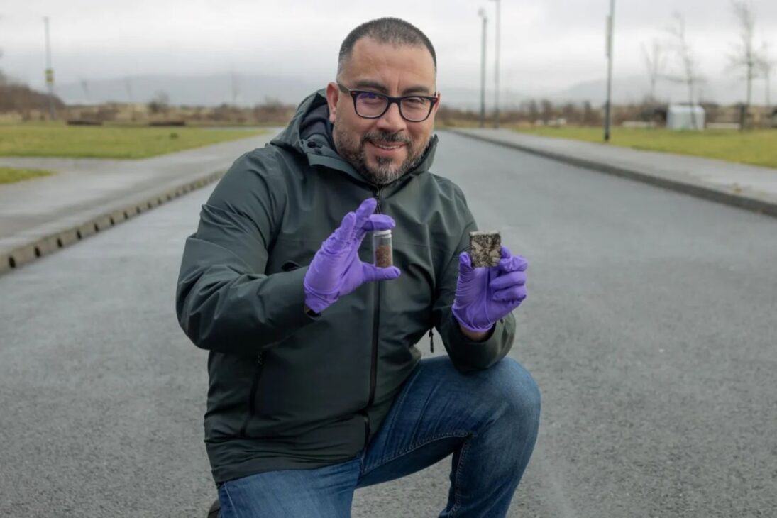 Investigador arrodillado en carretera asegurando muestras de asfalto autocurativo con guantes morados, demostrando tecnología innovadora de regeneración de pavimentos.