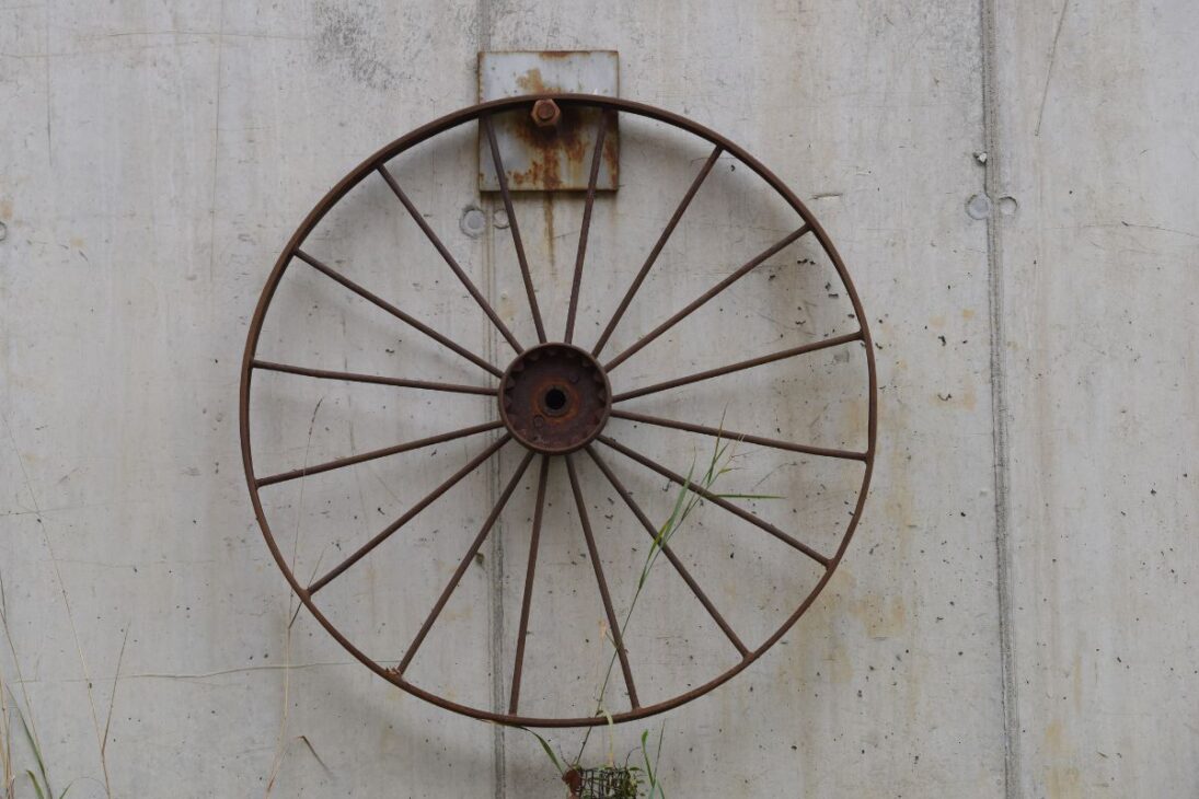 Rueda antigua de hierro con signos de óxido colgada en una pared de concreto, simbolizando el avance industrial y la durabilidad de los inventos.