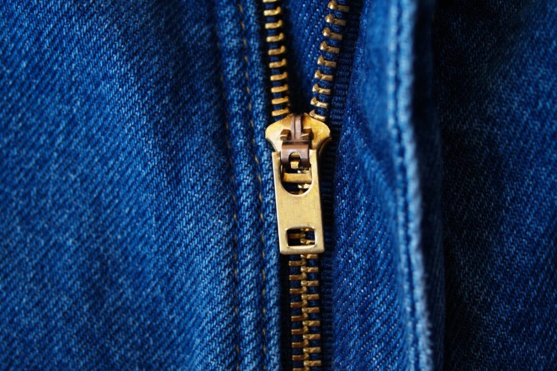Zíper de metal dorado en un pantalón vaquero azul, con costura contrastante y la textura del tejido denim en destaque.