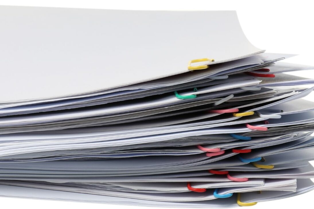 Una pila alta de papeles blancos, cada sección sujeta por clips de papel de colores diferentes, contra un fondo blanco.