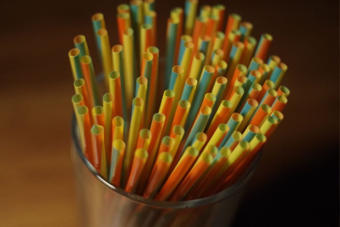 Enfoque de un vaso de vidrio con múltiples popotes de plástico coloridos y rayados.