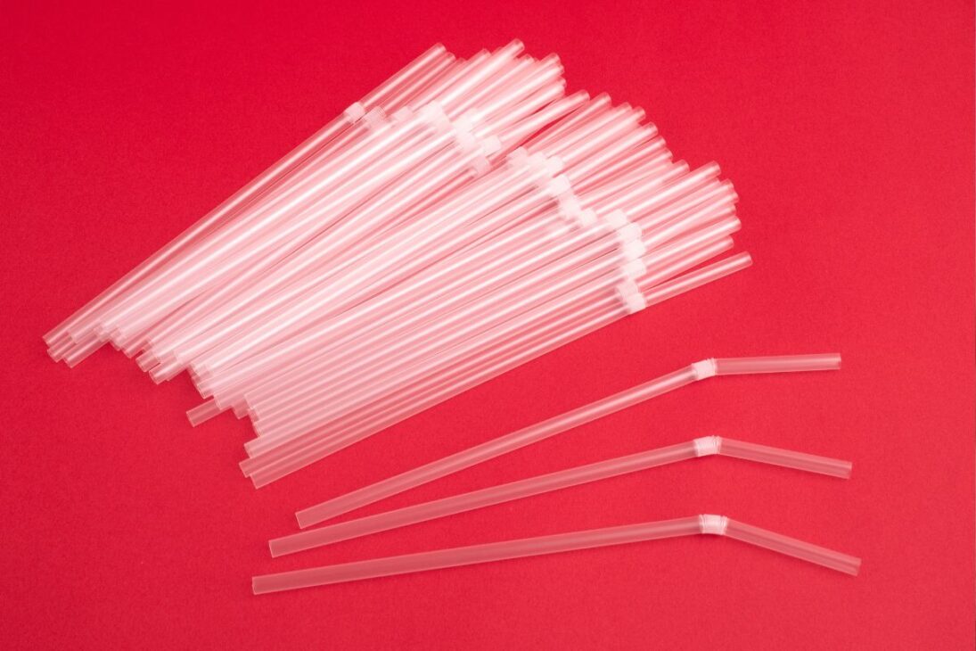 Montón de popotes de plástico transparentes y algunos con articulación doblable sobre un fondo rojo vibrante.