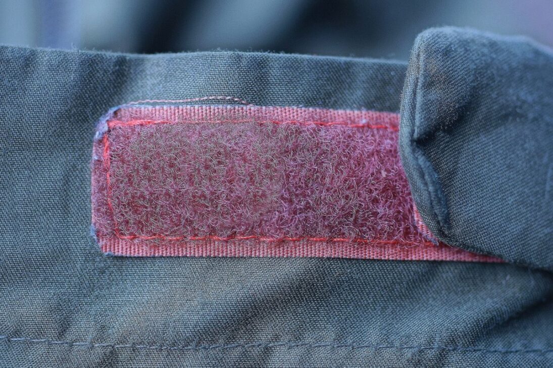 Close-up de un patch de velcro rojo cosido en tela verde, mostrando signos de uso.