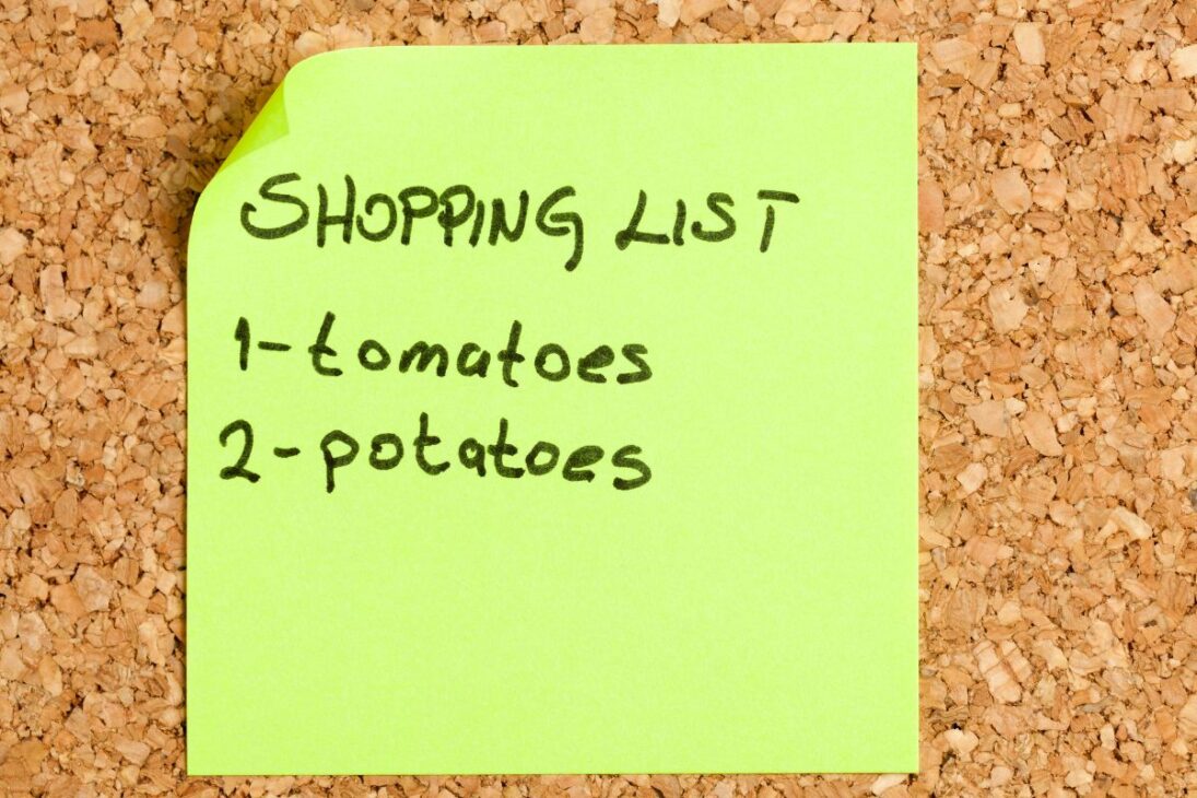  Post-it verde vibrante en un tablero de corcho, mostrando una lista de compras manuscrita.