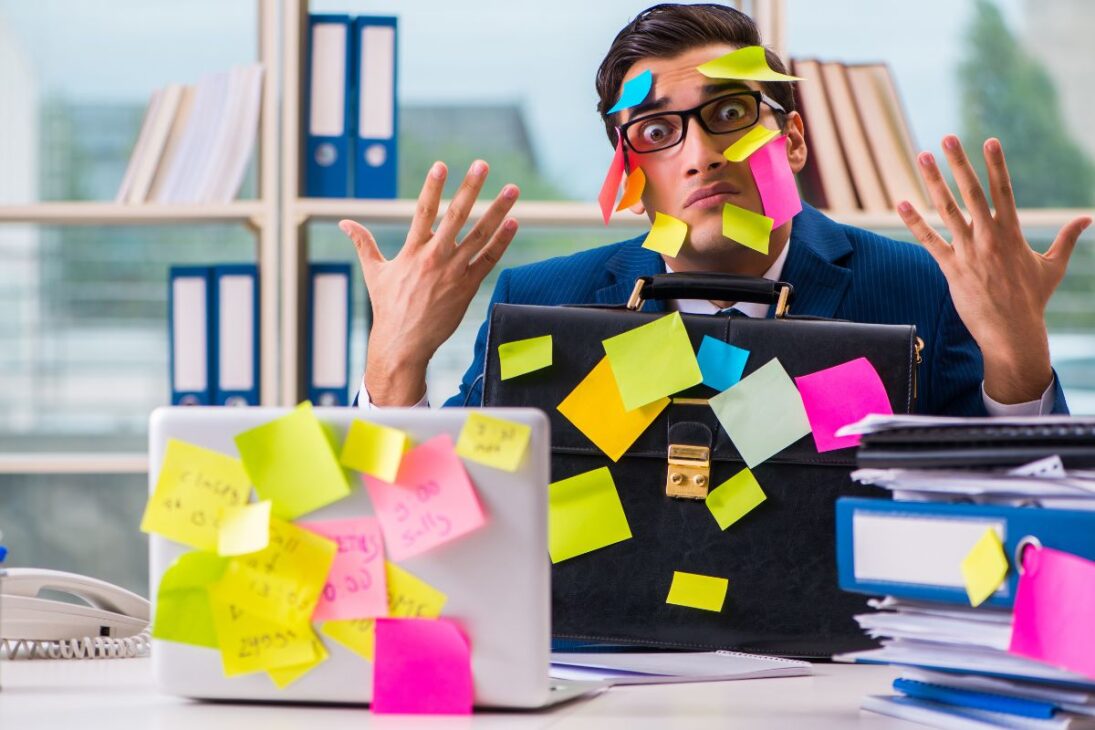 Hombre de negocios sobrecargado con post-its pegados en la cara y en objetos de oficina.