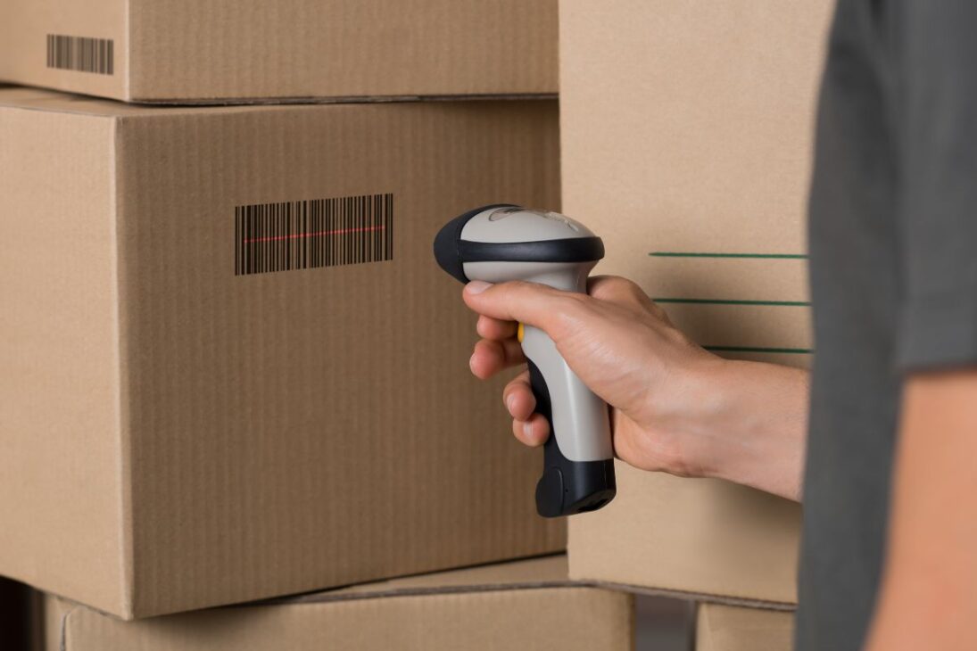 Mano sosteniendo un escáner de código de barras apuntando a cajas de cartón.