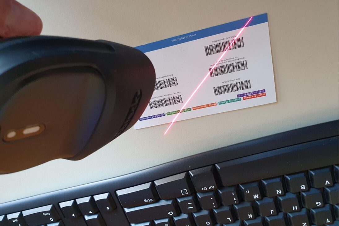 Escáner de código de barras portátil leyendo etiquetas en una tarjeta, con teclado visible.