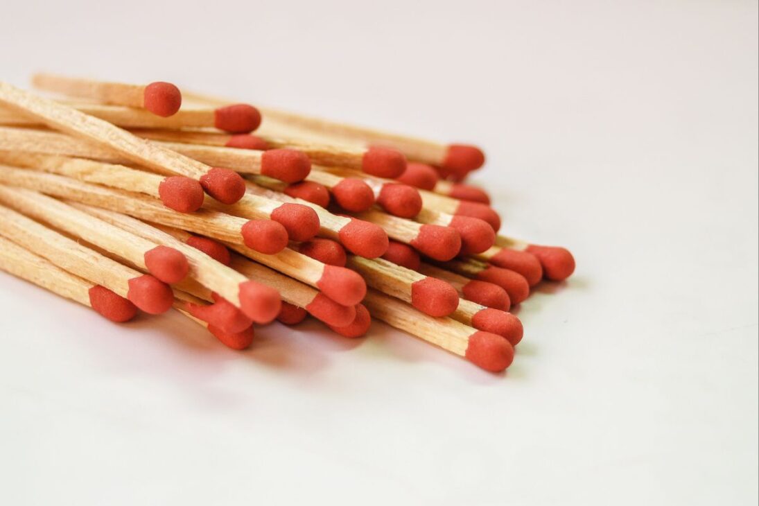 Un montón de fósforos de madera con puntas rojas agrupados sobre una superficie blanca.