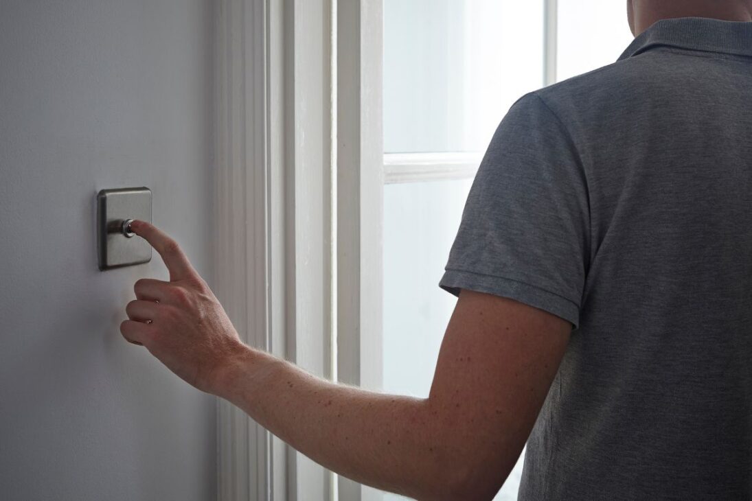 Hombre de espaldas presionando un interruptor de luz de metal cepillado con un botón giratorio.