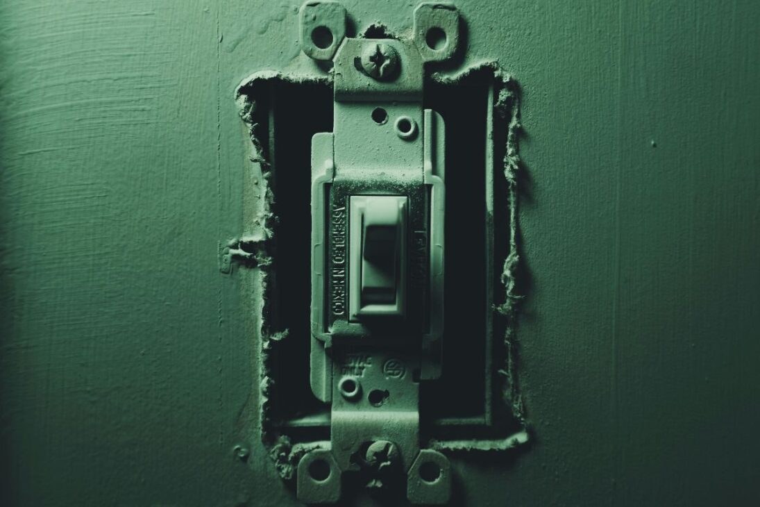 Interruptor de luz expuesto dentro de una caja de pared, con la pintura descascarándose alrededor.