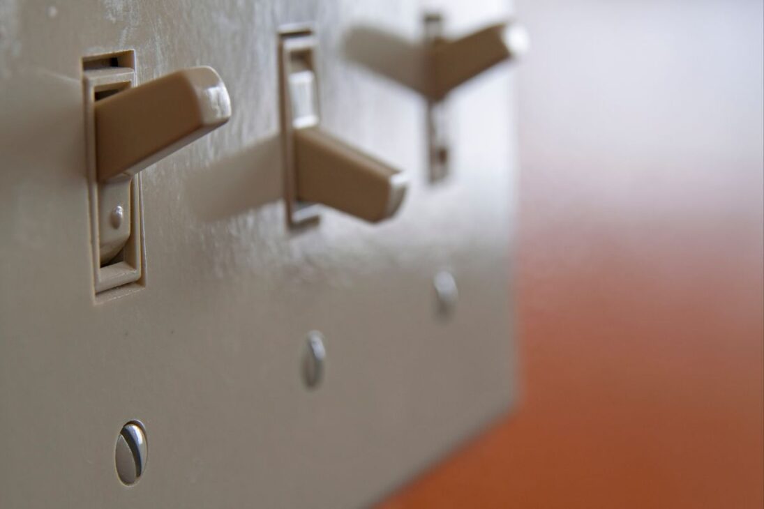 Tres interruptores de luz beige, estilo palanca, en una placa de pared, con los dos primeros en la posición "encendido" y el tercero parcialmente visible al fondo.