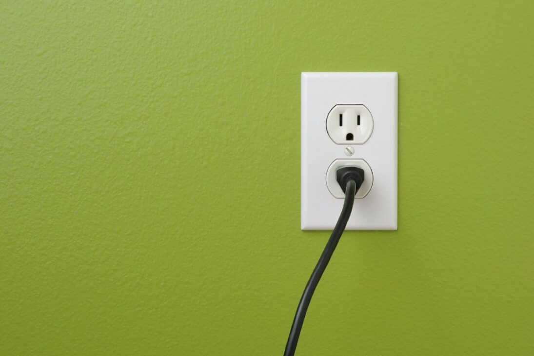 Enchufe negro insertado en la toma eléctrica blanca de tres orificios en una pared verde vibrante.