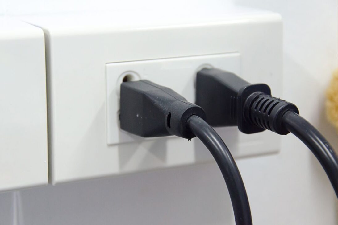 Dos enchufes negros conectados uno al lado del otro en una toma eléctrica doble de estándar Tipo N (brasileño).