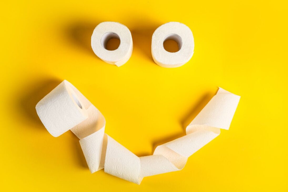 Rostro sonriente hecho con rollos y papel higiénico desenrollado en un fondo amarillo.
