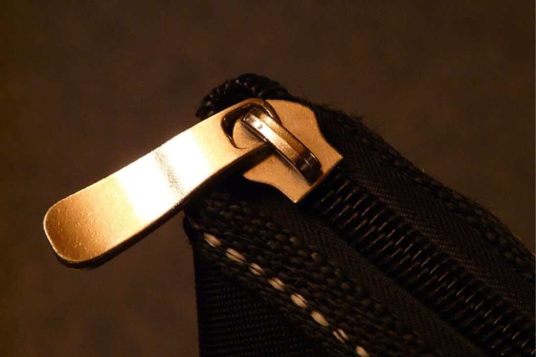 Cierre metálico dorado en primer plano, adherido a una tela negra texturizada, con luz cálida destacando el brillo del metal.