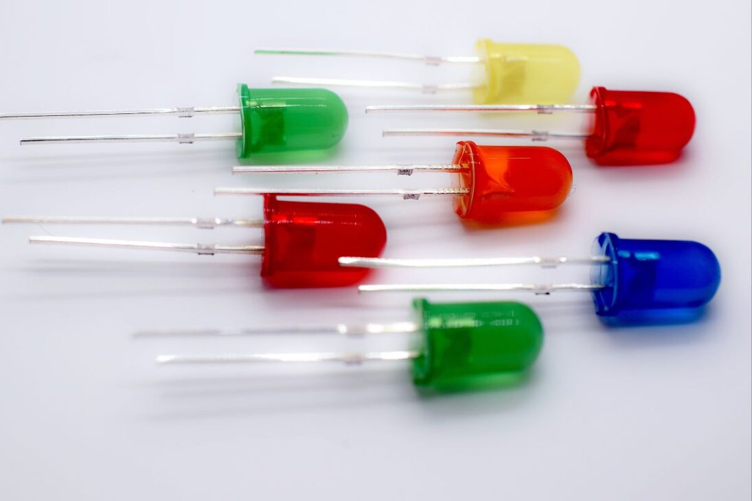  Una fila de diversos diodos emisores de luz (LEDs) de colores, incluyendo rojo, verde, azul y amarillo, dispuestos horizontalmente sobre una superficie blanca.