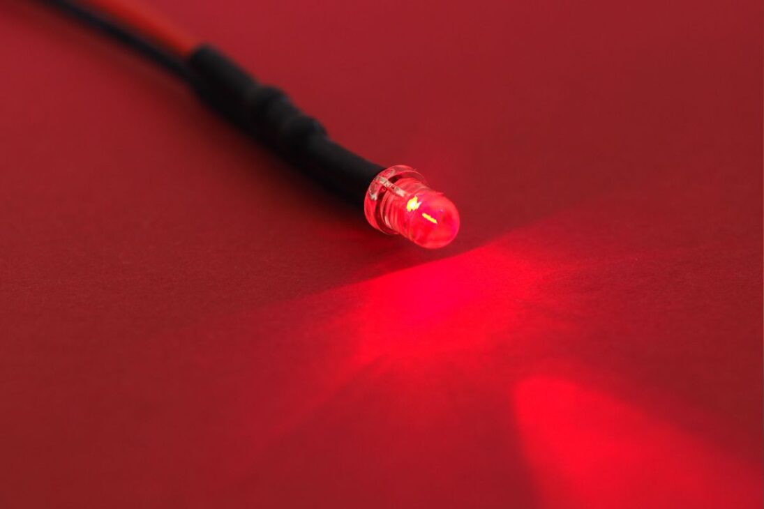 Un diodo emisor de luz (LED) rojo encendido, emitiendo un haz de luz vibrante sobre una superficie de papel rojo, con un cable negro conectado.
