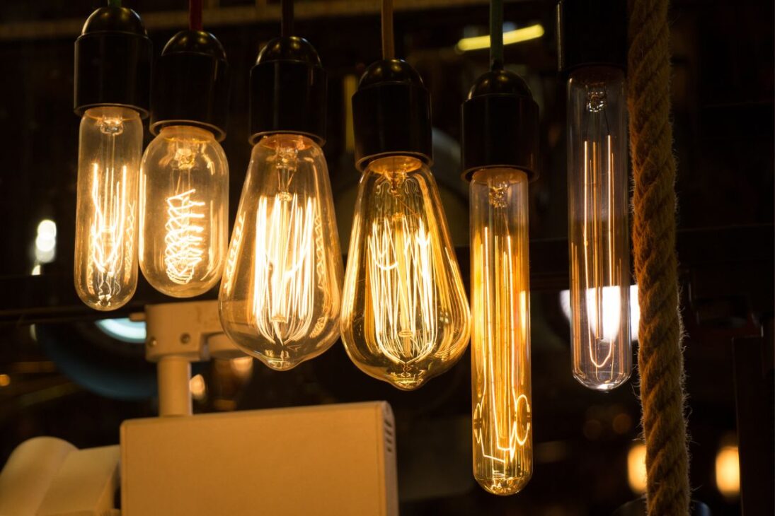 Seis lámparas de filamento estilo Edison colgadas, emitiendo un brillo cálido y naranja, contrastando con un fondo oscuro.