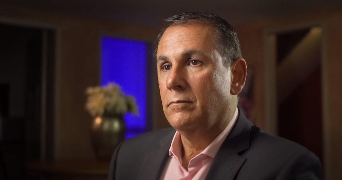 Homem de terno escuro em ambiente interno com iluminação suave e fundo desfocado.