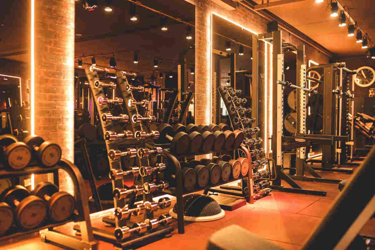 Academia de luxo com halteres organizados, iluminação amarela e ambiente moderno.