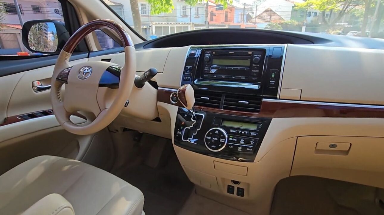 Panel frontal de la Toyota Previa 2018 con acabado beige y detalles en madera, volante multifuncional, cambio elevado y central multimedia analógica.
