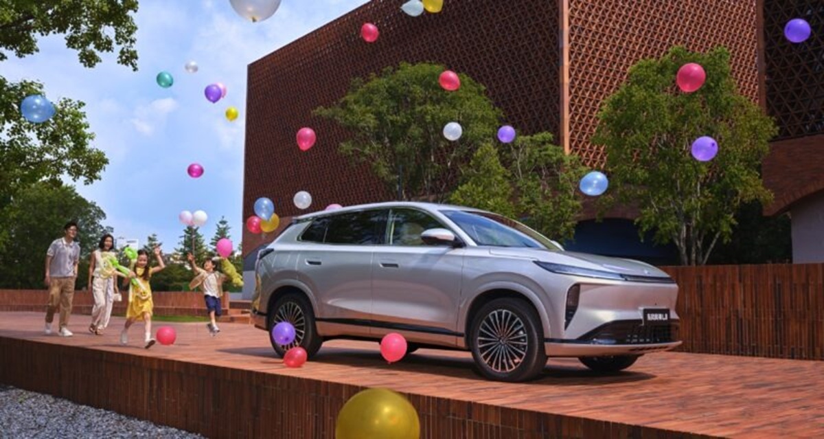 SUV elétrico híbrido chinês em exposição ao ar livre, com família ao fundo e balões coloridos, destacando novo lançamento automotivo.