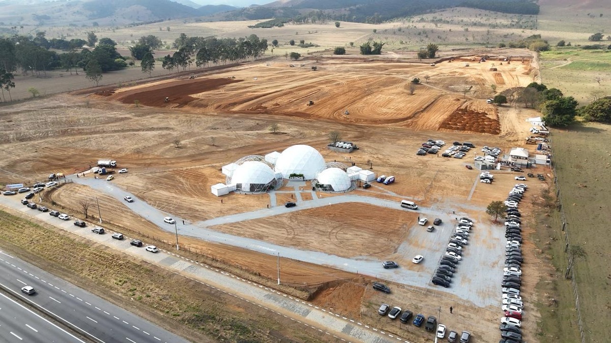 Vista aérea de terreno em fase de terraplanagem com estrutura geodésica da Hitachi ao centro e grande volume de veículos estacionados
