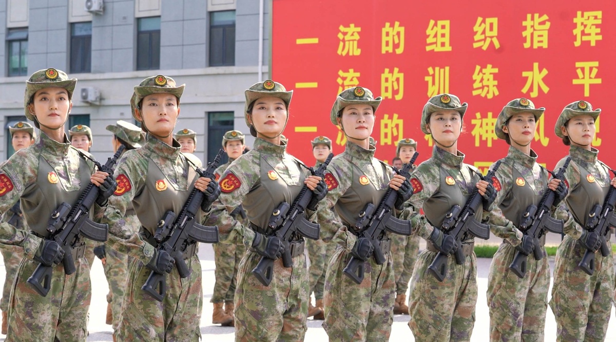 Soldadas chinesas em formação com fuzis modernos, em frente a um painel com inscrições em mandarim