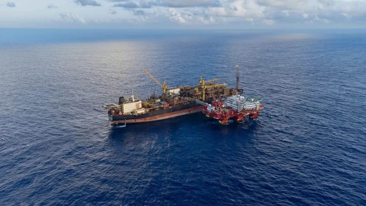 Plataforma de petróleo offshore com FPSO em operação no oceano, sob céu parcialmente nublado.