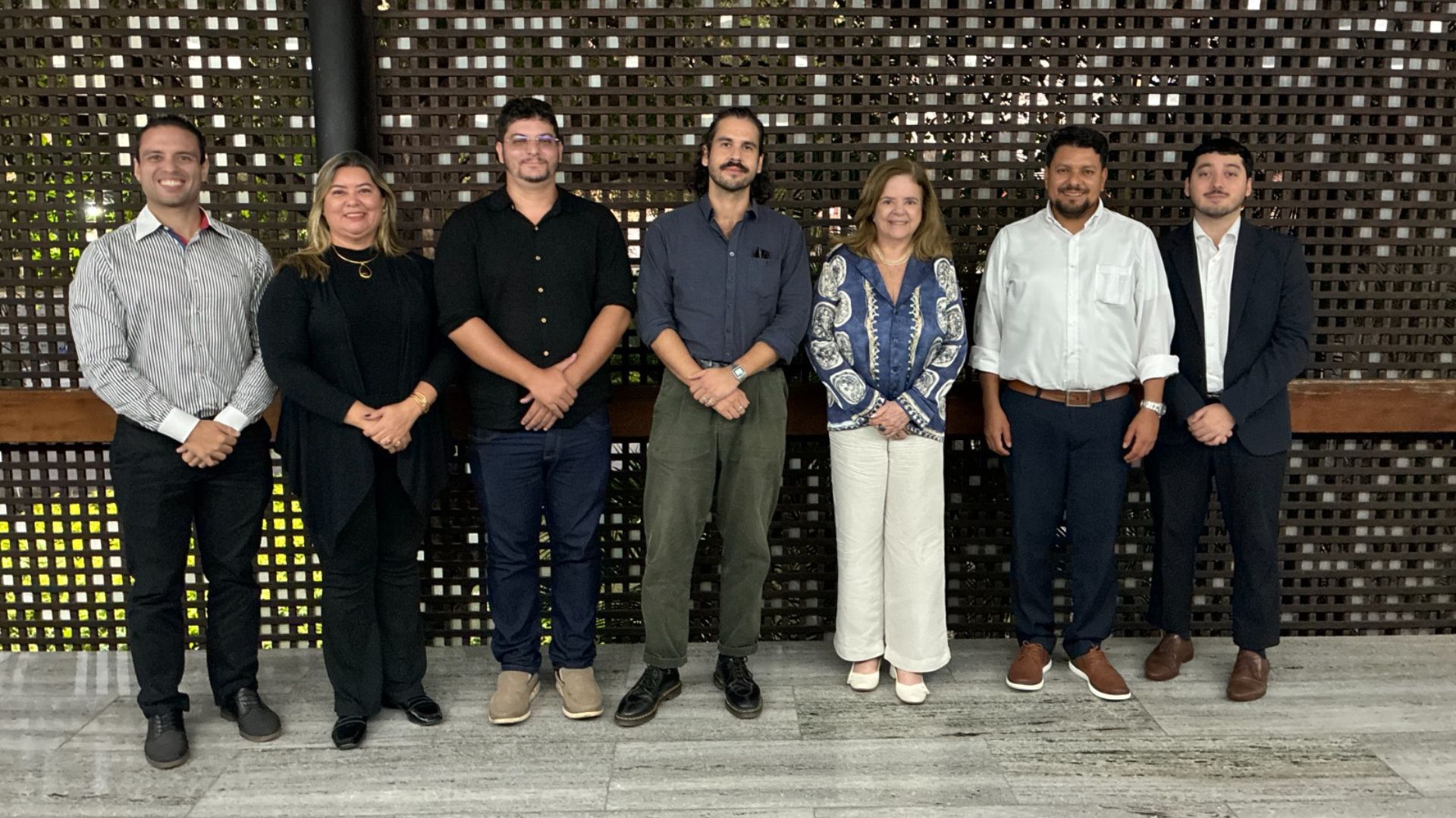 Grupo de sete profissionais em evento oficial posando diante de painel decorativo em ambiente corporativo