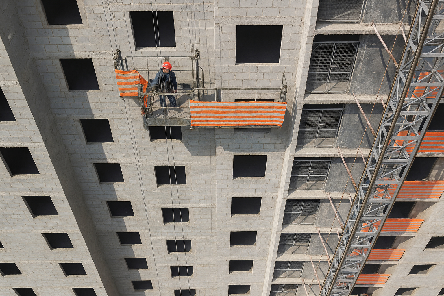 Operário em andaime realiza reforma em prédio habitacional com proteção laranja e grua lateral