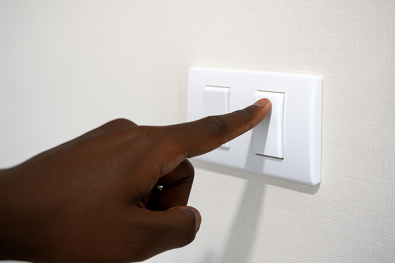 Mão de pele negra acionando interruptor de luz em uma parede branca.