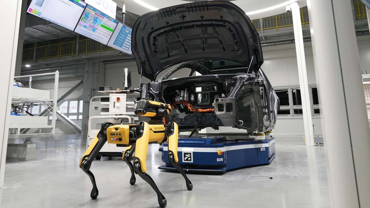 Spot olfateando un vehículo eléctrico parcialmente montado, ilustrando la combinación de robots avanzados con inspección automotiva de precisión.
(Imagen: MotorTrend — fábrica inteligente con perros-robots en acción)