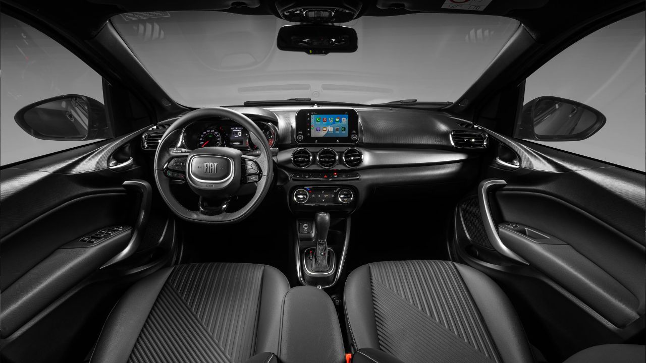 A pesar de recibir mejoras puntuales en el acabado, como el techo negro y revestimiento sintético, el interior del Fiat Cronos 2026 aún denuncia la edad del proyecto al mantener la central multimedia de 7 pulgadas y no ofrecer ajuste de profundidad en el volante.