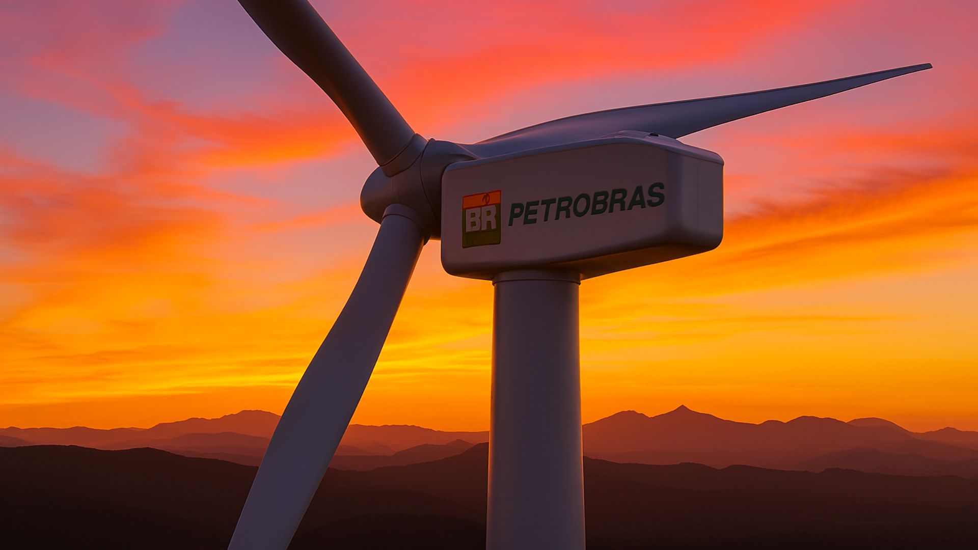 Turbina eólica de grande porte com logotipo da Petrobras, ao pôr do sol, em cenário montanhoso.