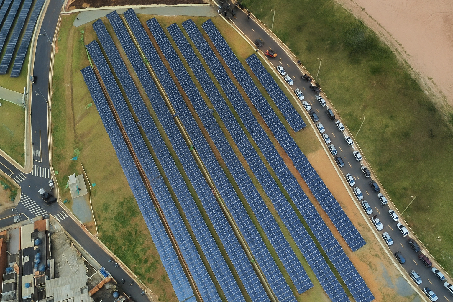 Vista aérea aproximada de usina solar com várias fileiras de painéis fotovoltaicos instalados em terreno amplo.