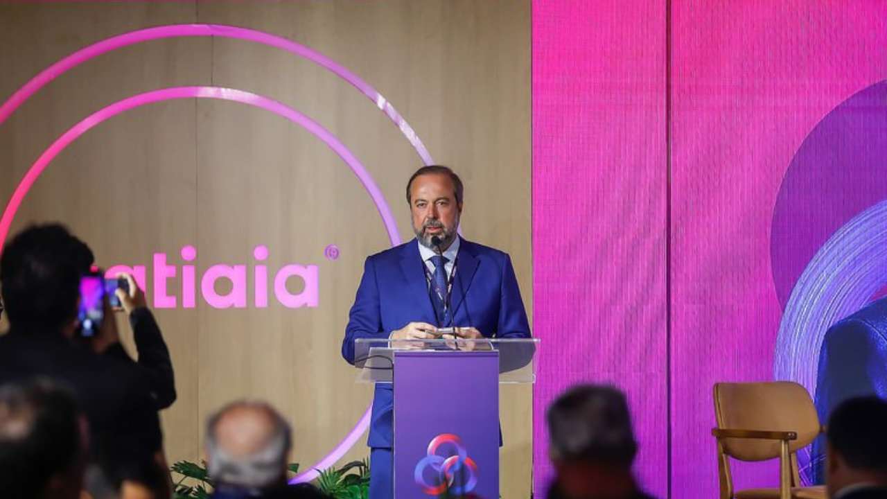 Silveira de terno azul discursando em um púlpito transparente durante evento formal, com fundo iluminado e logotipo “itatiaia” ao fundo.