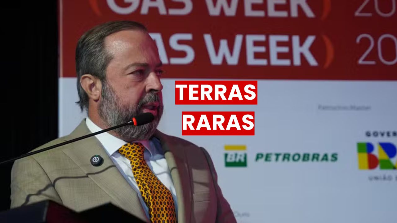 Silveira com terno bege e gravata estampada fala em evento oficial sobre terras raras, com banner da Petrobras e Governo Federal ao fundo