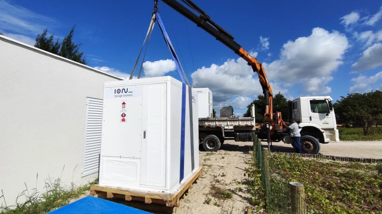 Container branco da ION Storage Solutions sendo instalado com guindaste em área externa, representando tecnologia de armazenamento de energia.