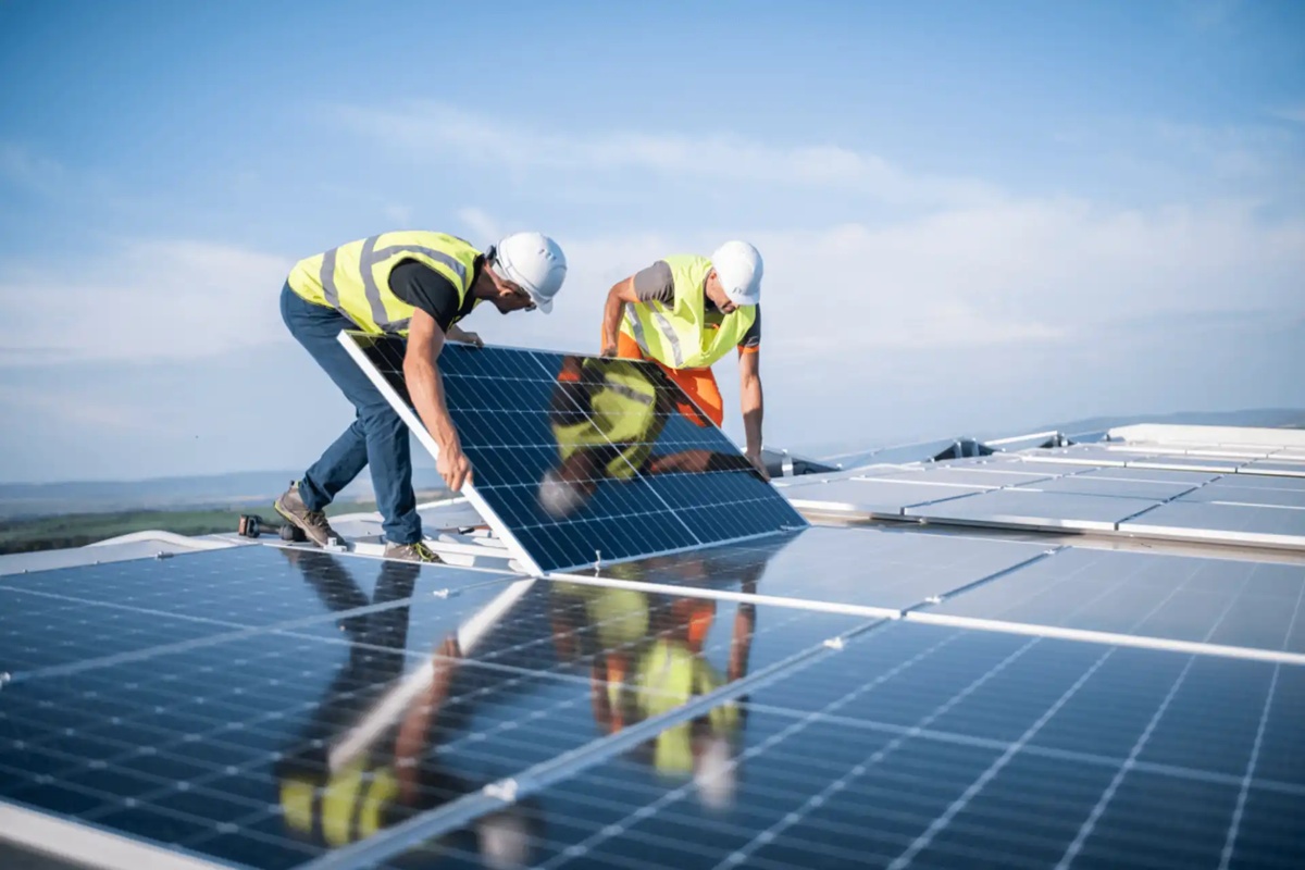 Técnicos instalam painéis solares em telhado sob céu limpo