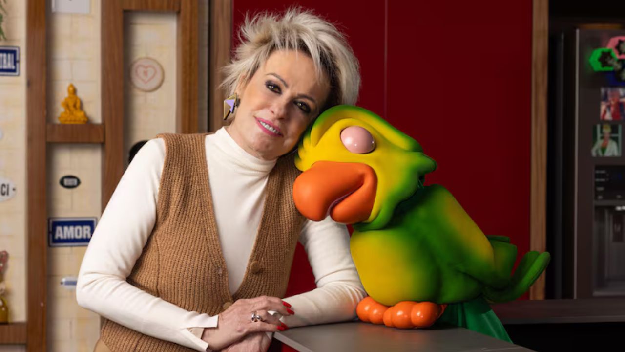 Ana Maria Braga posa sorridente ao lado de Louro Mané, o carismático papagaio do programa Mais Você, em um ambiente acolhedor e repleto de símbolos afetivos.