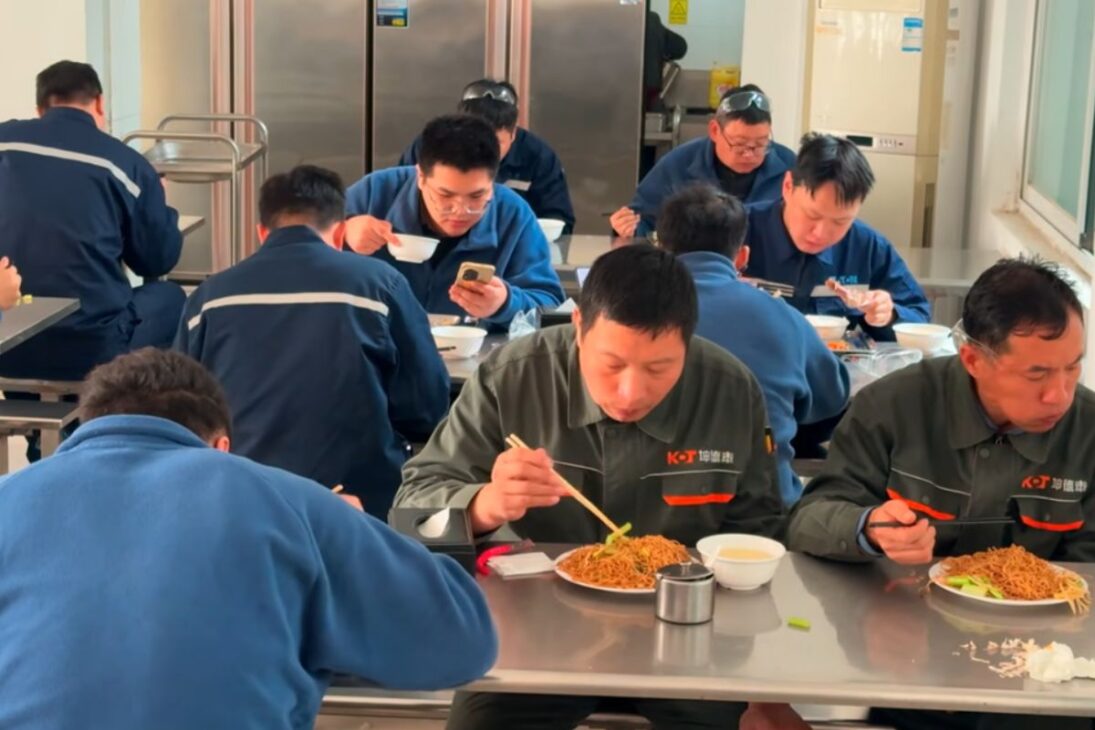 En el comedor de la fábrica china, bandejas de metal sirven almuerzo caliente con fideos al vapor, pollo Kung Pao y rutina intensa de producción para cientos de trabajadores.