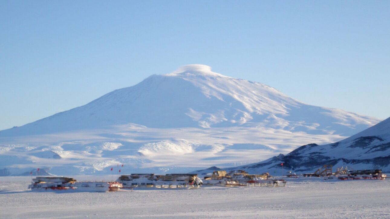 Paisaje de la Isla Ross con la base McMurdo y el volcán activo al fondo, escenario de la Antártida. (Imagen: Estación McMurdo vista con el Monte Erebus al fondo y el hielo alrededor)