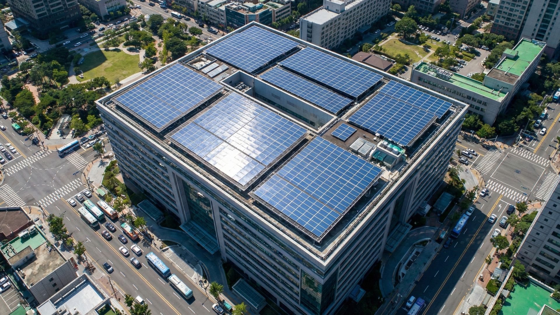 Vista aérea de prédio urbano com telhado coberto por painéis solares, cercado por ruas e áreas verdes