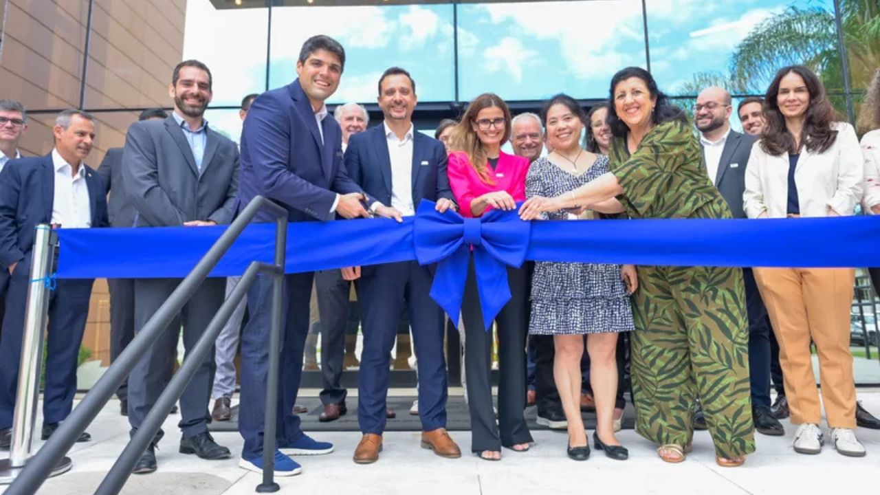 Cerimônia de inauguração com grupo de profissionais cortando uma fita azul diante de um prédio moderno envidraçado.