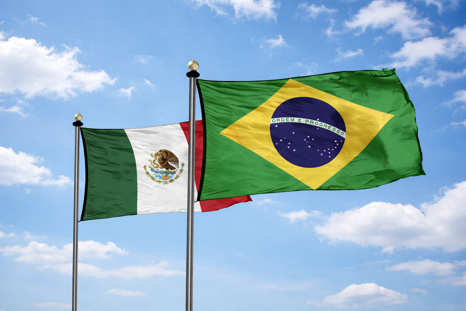 Bandeiras do Brasil e do México hasteadas lado a lado, tremulando ao vento sob um céu azul com nuvens leves.