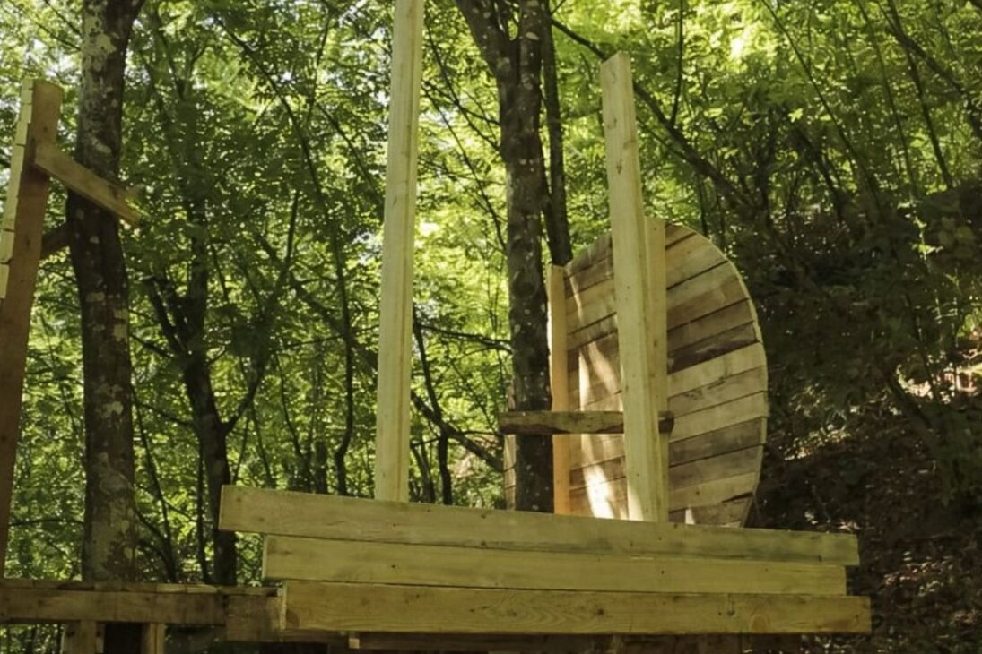 Toca hobbit en esfera de madera hecha con palets de madera, techo de musgo y casa en árbol que se integra al bosque.