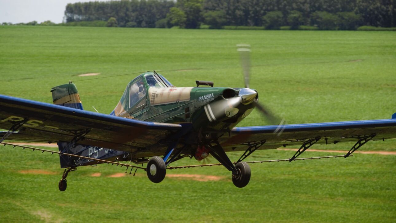 El Avión Agrícola Ipanema De Embraer En Vuelo Bajo Sobre Cultivo, Con Hélice En Movimiento Y Barras De Pulverización Visibles Durante La Operación En El Campo.