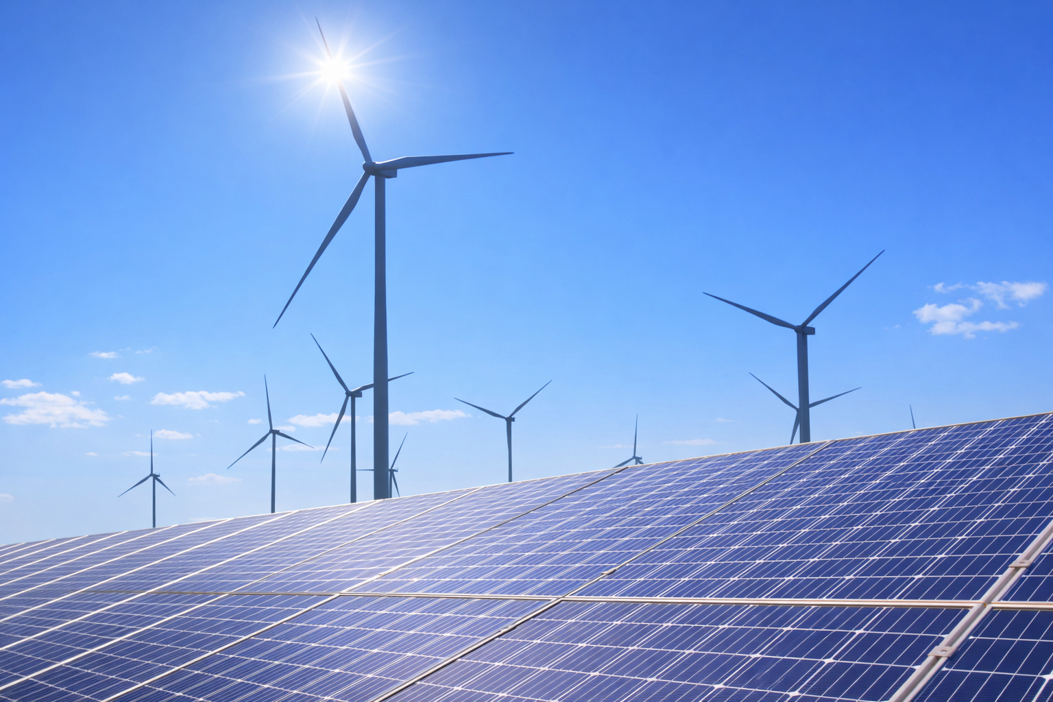 Painéis solares em primeiro plano e turbinas eólicas ao fundo sob céu azul de meio-dia, representando geração de energia renovável.