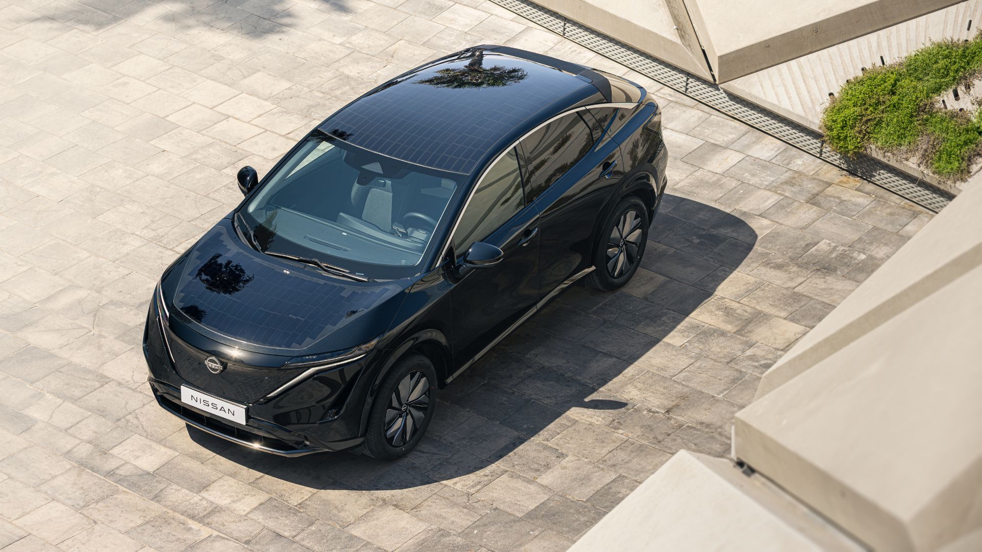 SUV elétrico Nissan Ariya visto de cima, com painéis solares integrados ao teto, estacionado em área urbana moderna durante o dia